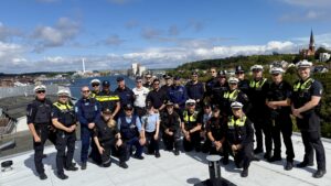 Eine große Gruppe mit unterschiedlichen Uniformen steht auf einem hohen Dach, Im Hintergrund die Flensburger Förde